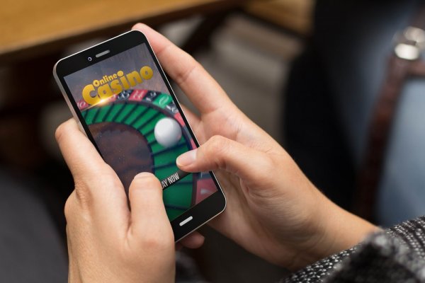 Händer som håller mobil med rouletthjul på online casino